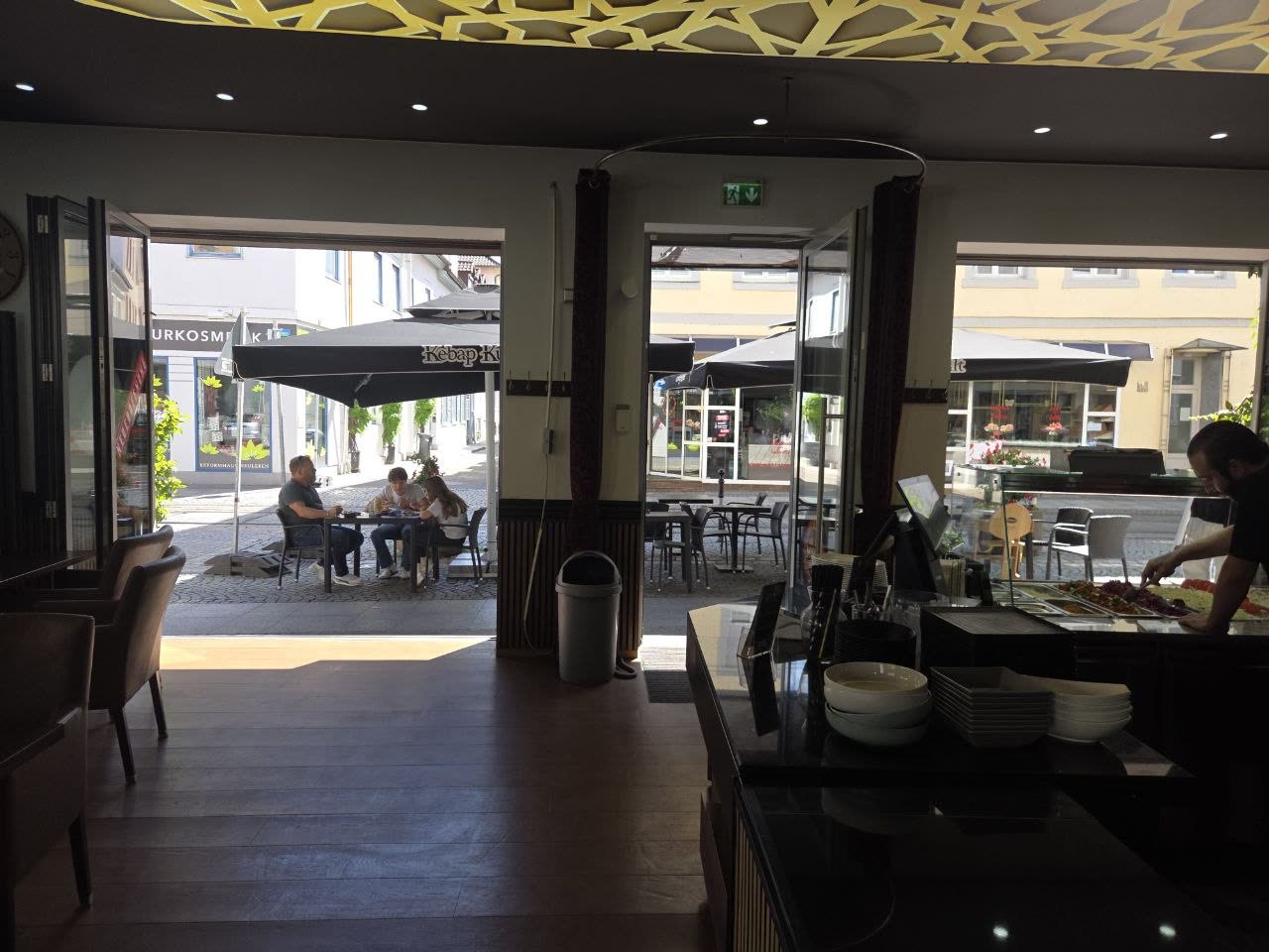 Blick aus dem Innenraum hinaus auf die Terrasse und die Gasse