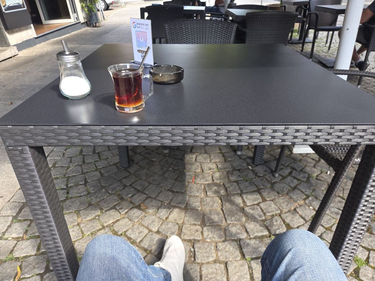 Ein Glas Çay auf einem Tisch der Terrasse, darunter das Kopfsteinpflaster der Pfinztalstraße