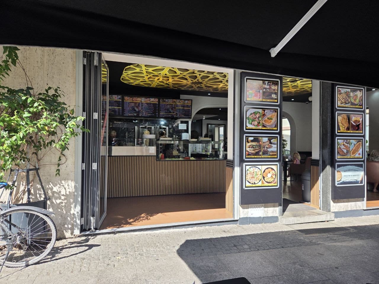 Das Miros Grill Haus von der Pfinztalstraße aus, mit geöffneten Falttüren und Markise